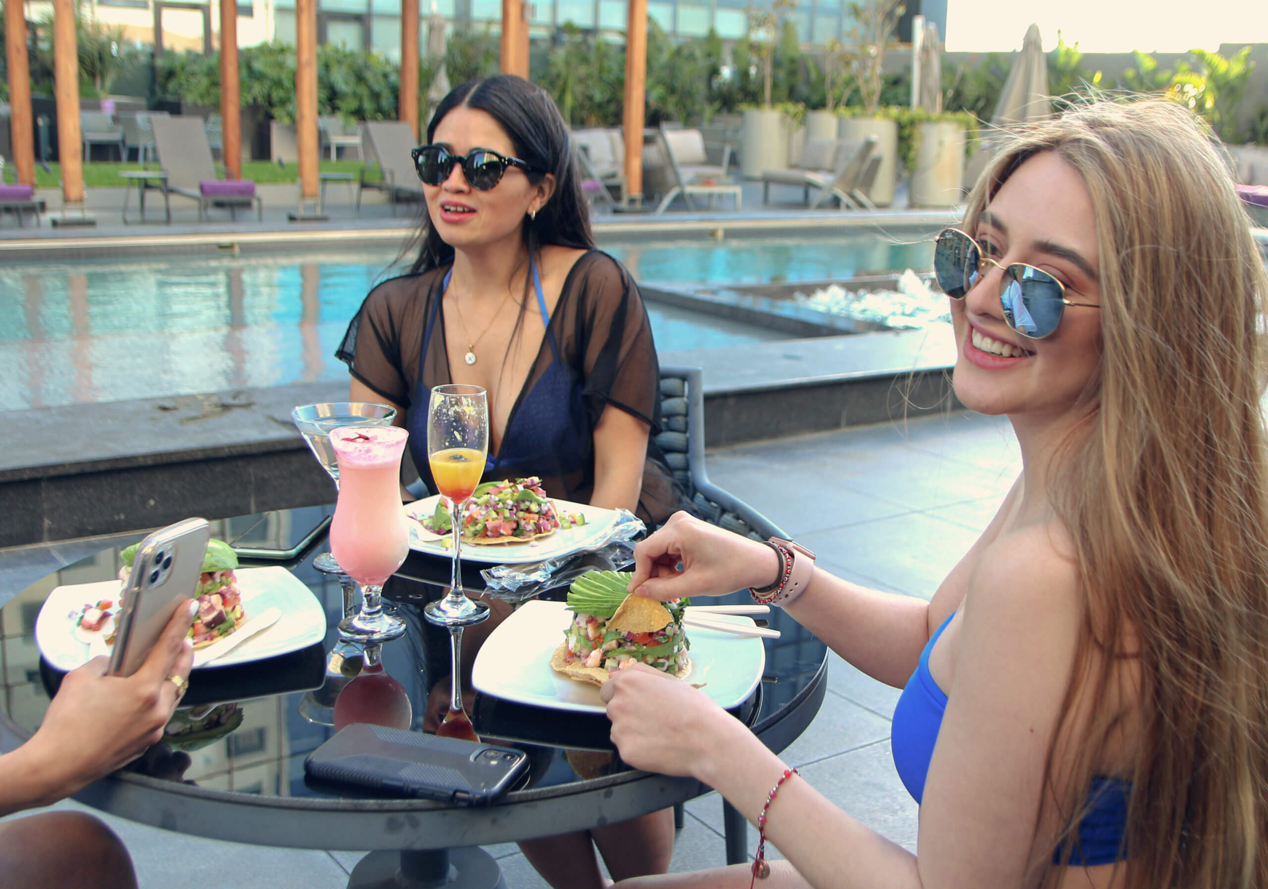 Women enjoying a leisurely lunch by the pool at Quartz Hotel Tijuana, sitting around a table with food and drinks in a serene outdoor setting.