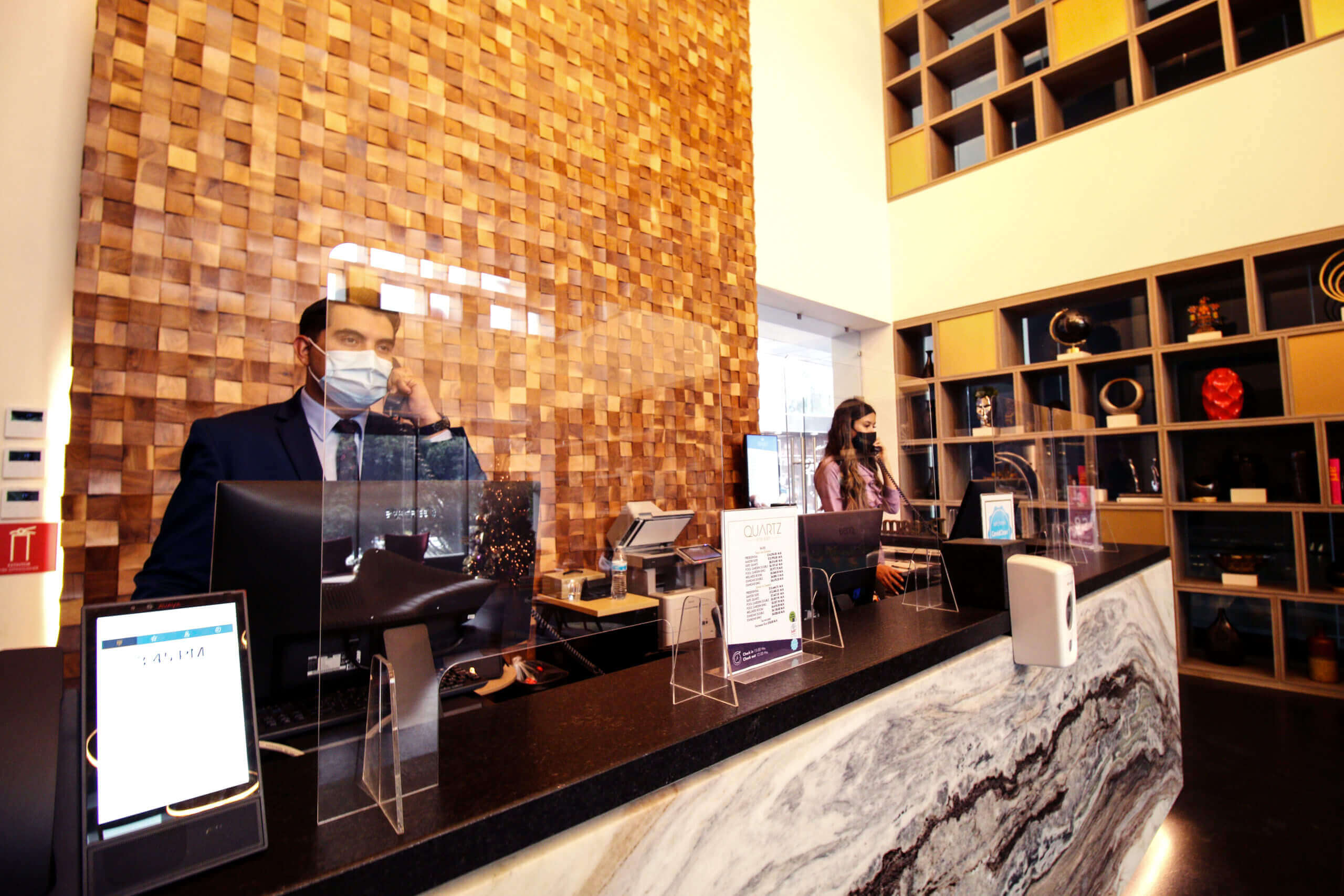 Man standing at the sleek, modern reception desk of Quartz Hotel Tijuana, greeted by friendly staff in a stylish lobby with contemporary design elements.